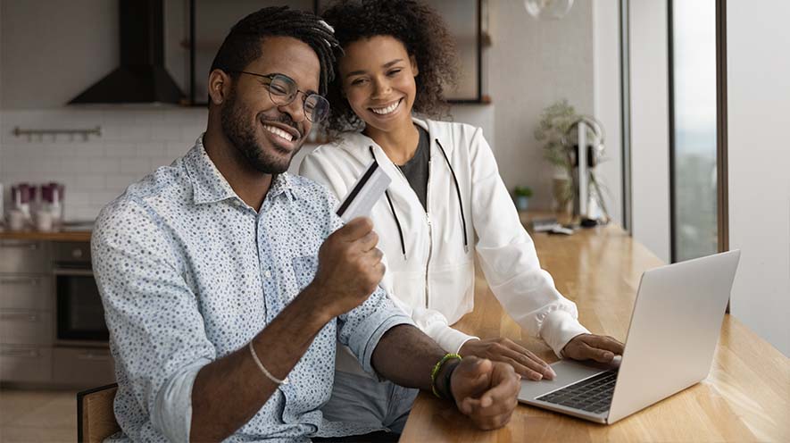 man holds credit card while sitting next to woman at computer