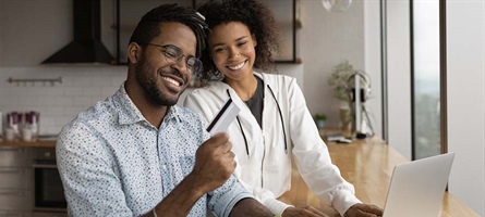 man holds credit card while sitting next to woman at computer