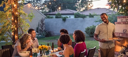 men and women gathered around a table, eating at an outdoor bqq-style party