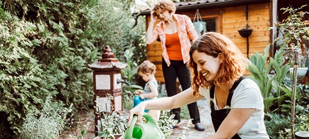 Women waters plants as child and another woman are in backyard