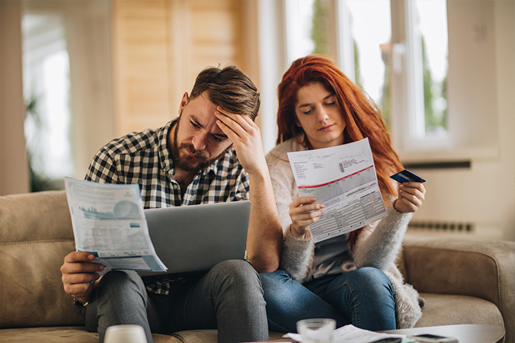 Man and woman on couch appearing stressed while staring at papers.