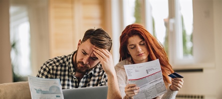 Man and woman on couch appearing stressed while staring at papers.