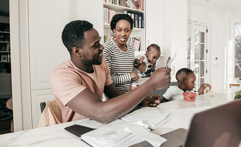 man and woman look at computer while holding young children