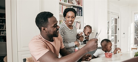 man and woman look at computer while holding young children