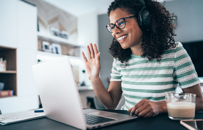 Woman with headset waves at computer screen