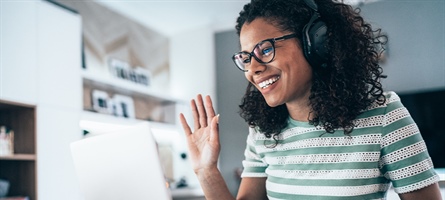 Woman with headset waves at computer screen