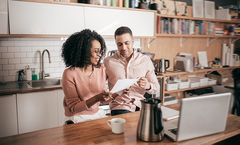 Man and woman looking at paper, sitting in front of computer