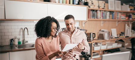 Man and woman looking at paper, sitting in front of computer