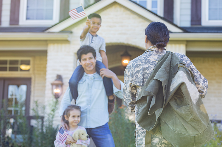 Woman in camo greets man, boy and girl holding flags and smiling