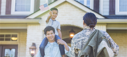 Woman in camo greets man, boy and girl holding flags and smiling