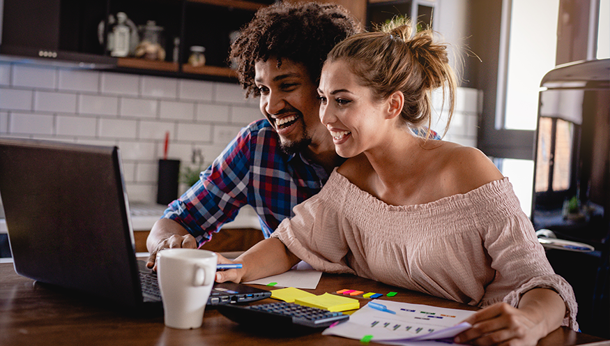 Man and woman sitting at computer paying bills and smiling