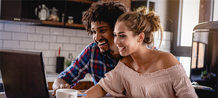 Man and woman sitting at computer paying bills and smiling