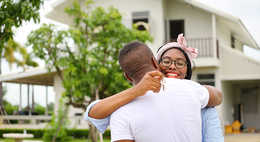 Woman holds key to new home as she hugs a man in the front yard of the house.