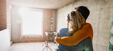 Man and woman hug as they stare at empty room under construction