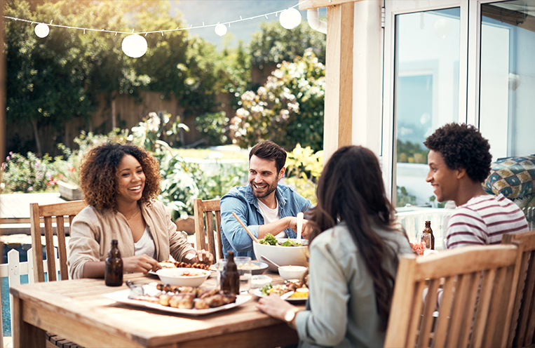 Four people eating, drinking and conversing together at outdoor table setting.