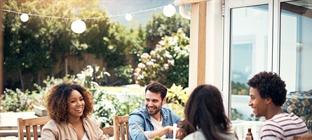 Four people eating, drinking and conversing together at outdoor table setting.