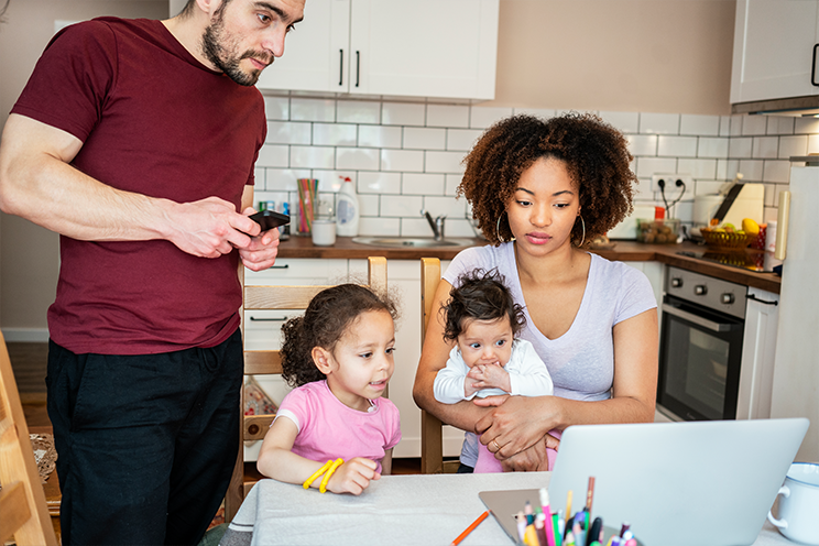 Man, woman and two young children huddle together in a kitchen, staring at a computer screen