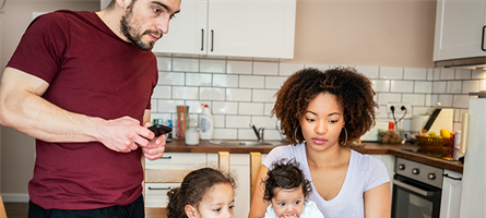 Man, woman and two young children huddle together in a kitchen, staring at a computer screen