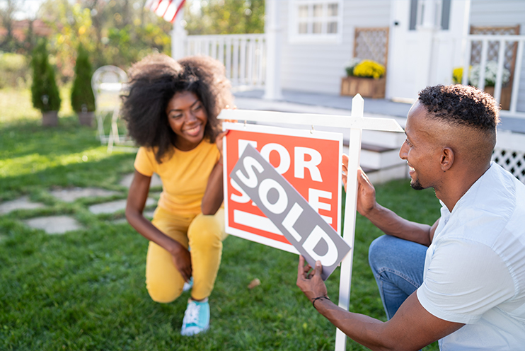 Man and woman stand in front of For Sale sign with a Sold sign above it