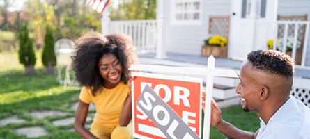 Man and woman stand in front of For Sale sign with a Sold sign above it