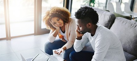 man and woman sitting on couch staring at computer, appearing distressed and downtrodden