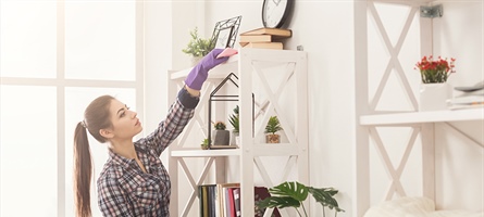 woman with cleaning gloves is dusting a shelf