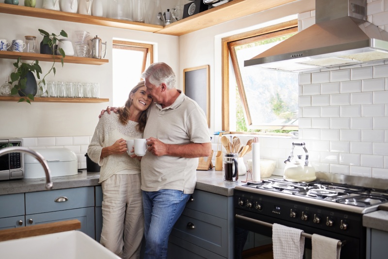 A couple embracing in their kitchen drinking coffee