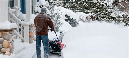 Man is using a handheld snowplow to rid his home's walkway of deeply covered snow.