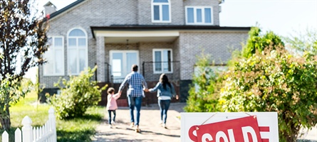 Family walks toward new home with sold sign at the forefront